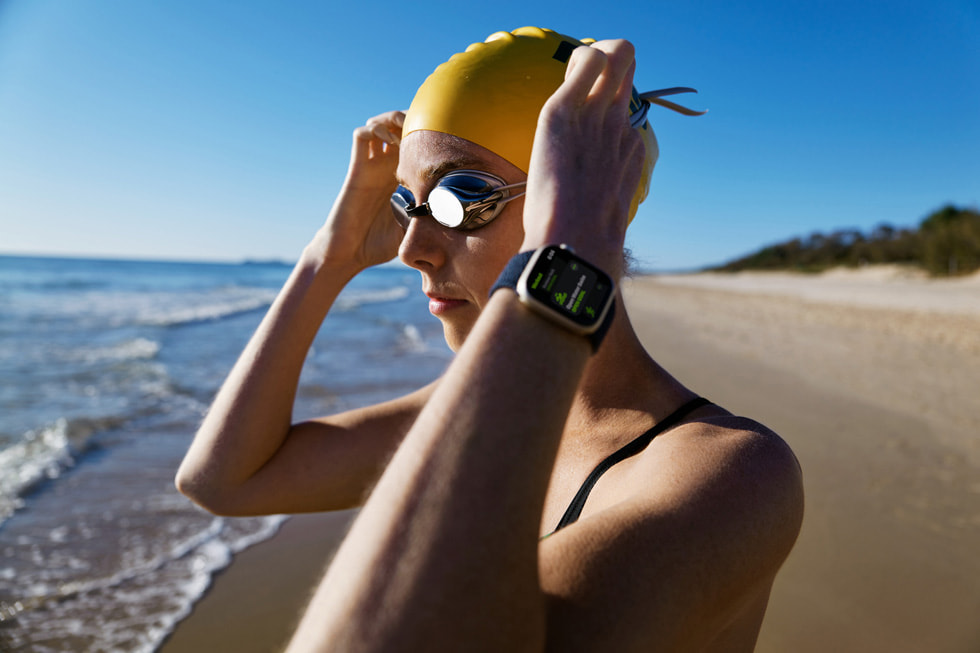 Kareena Lee by the ocean with her Apple Watch, adjusting her swim cap.