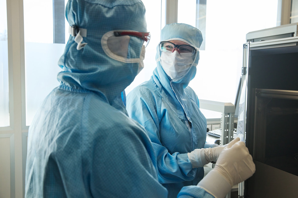 To teknikere hos TRUMPF Ditzingen iført beskyttelsestøj kigger på hinanden i laboratorie-lignende omgivelser.