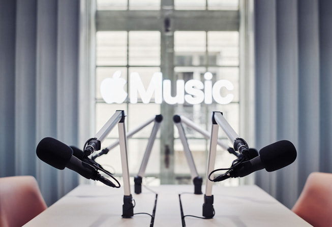 Deux micros sont posés sur une table de conférence face à une fenêtre portant un panneau Apple Music.