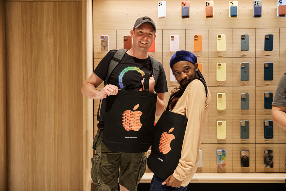 Hai khách hàng đang tạo dáng với túi tote của cửa hàng Apple Battersea.