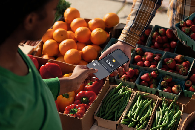 At a farmer’s market, a merchant is shown using the Tap to Pay on iPhone capability with a customer.