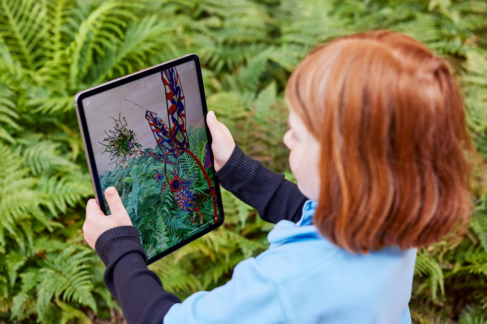 Une jeune élève tient un iPad Pro à bout de bras pour observer la flore en extérieur à travers l’app Deep Field.