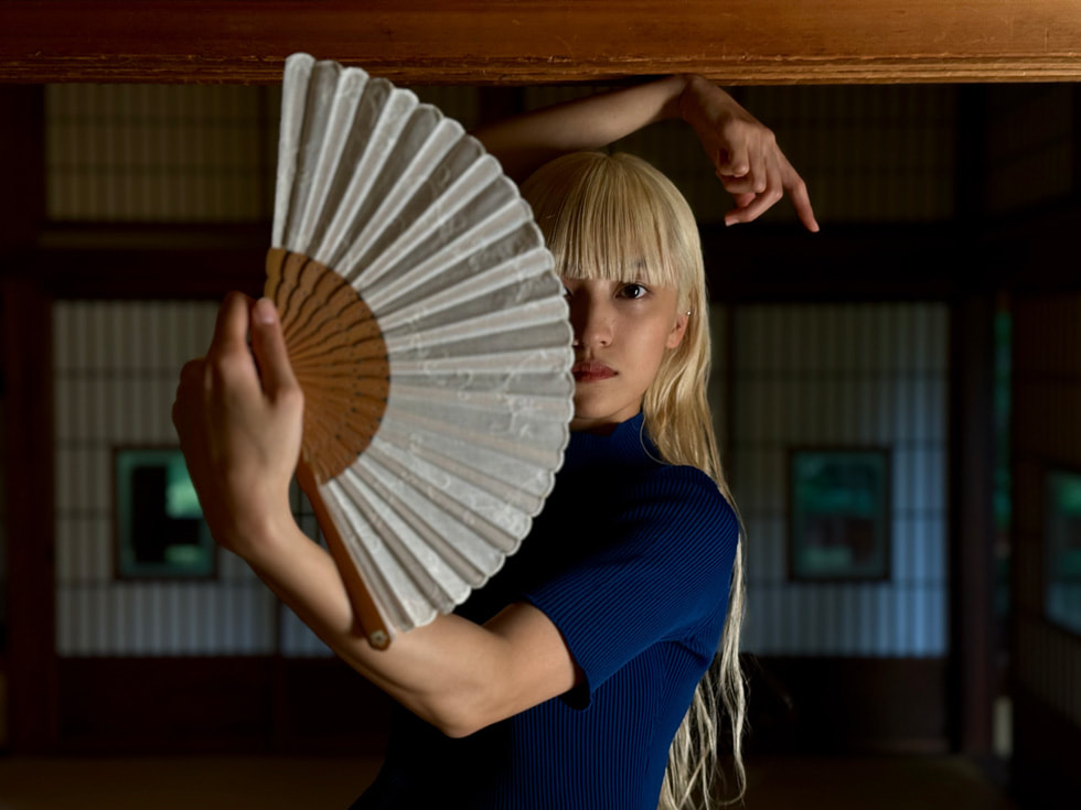 A woman with a fan captured in Portrait mode on iPhone 15 Pro Max.