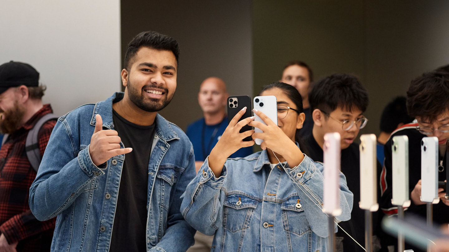 Two customers smile and hold up two iPhone devices inside Apple Sydney, Australia.