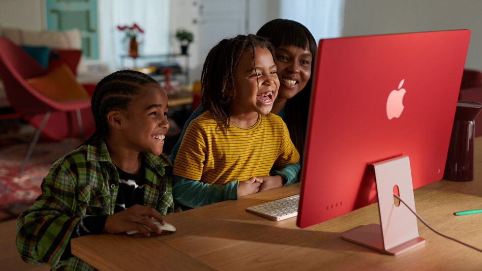 Duas crianças e uma pessoa adulta da família usam o novo iMac com chip M3 em rosa com teclado e mouse na mesma cor.