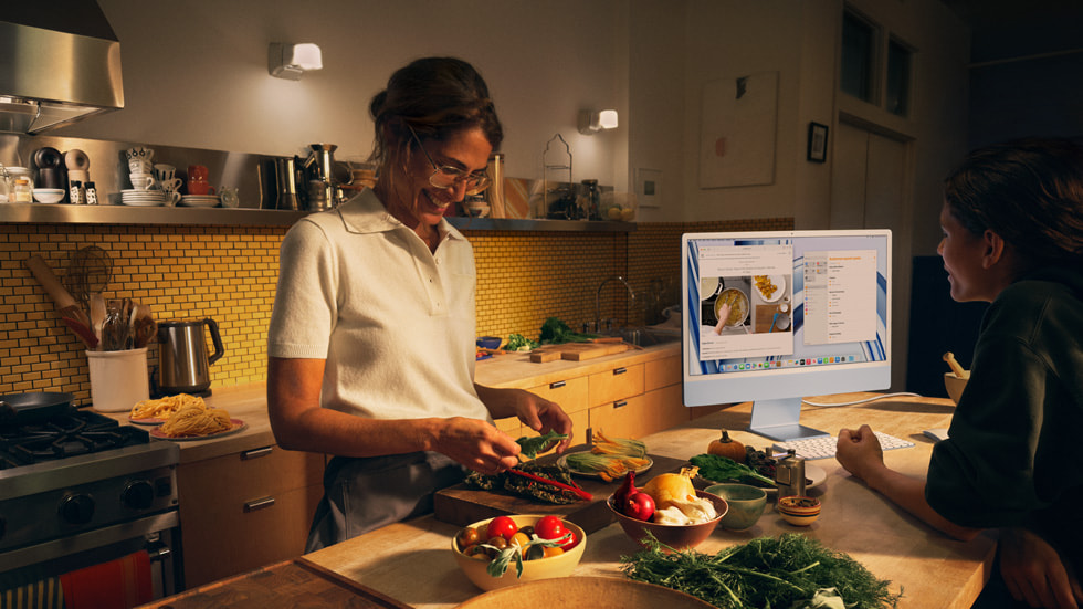 En vuxen och ett barn som lagar mat i ett kök och använder nya iMac med M3 i blått med tangentbord och mus i matchande färg.