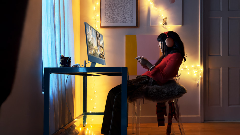 Une personne joue aux jeux vidéo sur le nouvel iMac avec puce M3 en portant des AirPods Max de couleur rouge.