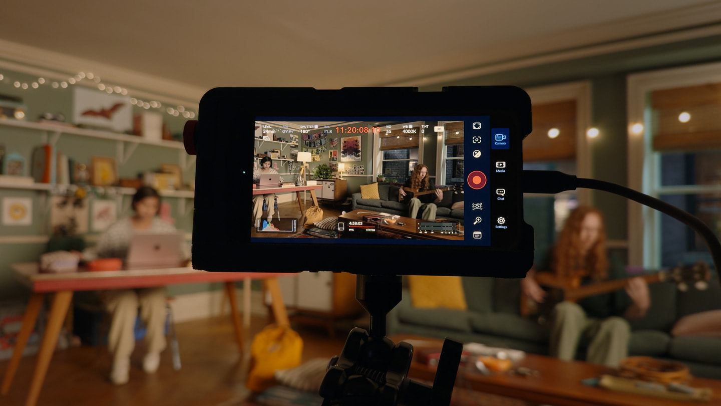 An iPhone 15 Pro Max on a rig captures a person sitting at a desk working on a MacBook.