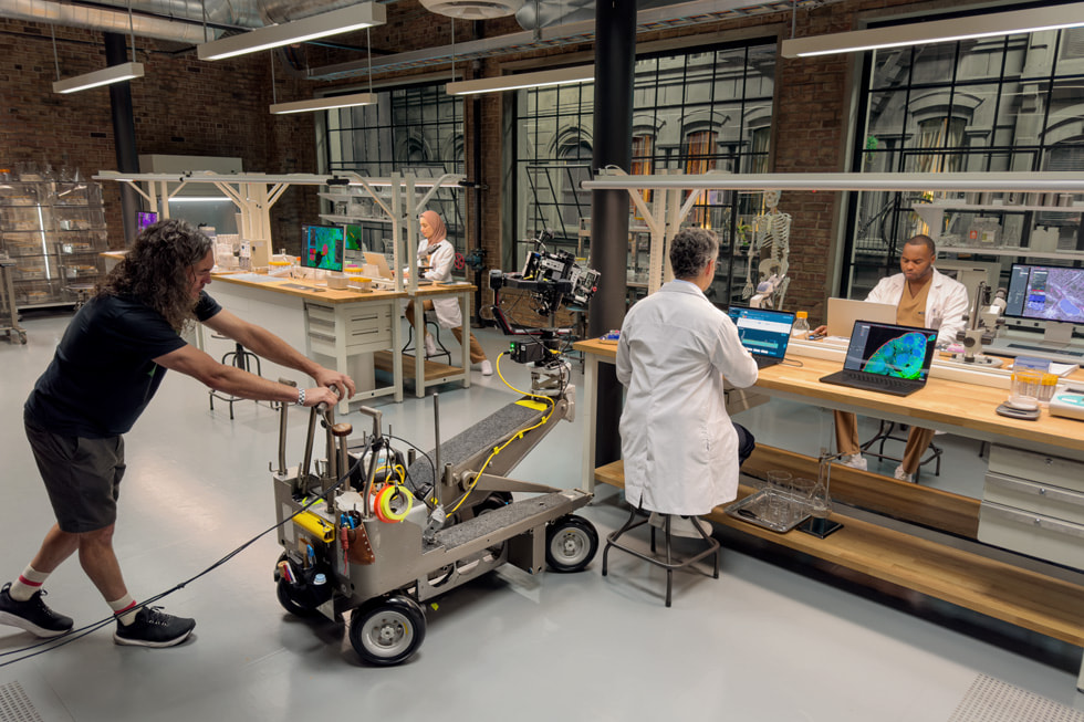 Sur le tournage, un iPhone 15 Pro Max sur un chariot filme le MacBook Pro dans un décor médical afin de présenter les nouvelles fonctionnalités destinées aux professionnels de santé.