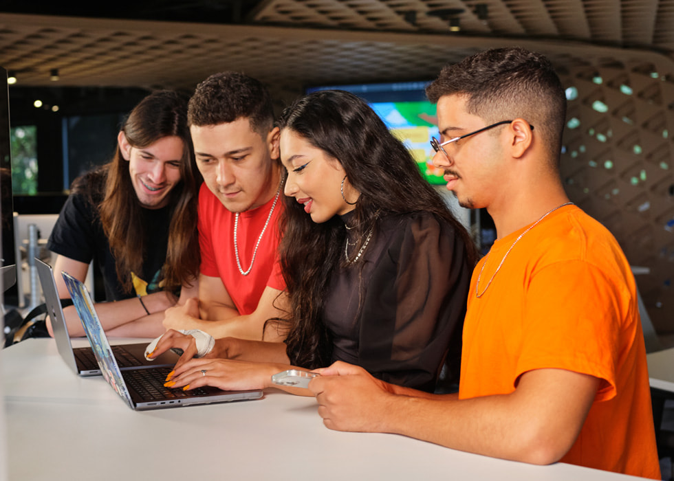 Um grupo de estudantes reunidos em volta de uma pessoa que está usando um MacBook Pro.