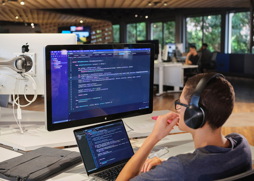 Estudante programando em um MacBook Pro conectado a um iMac.