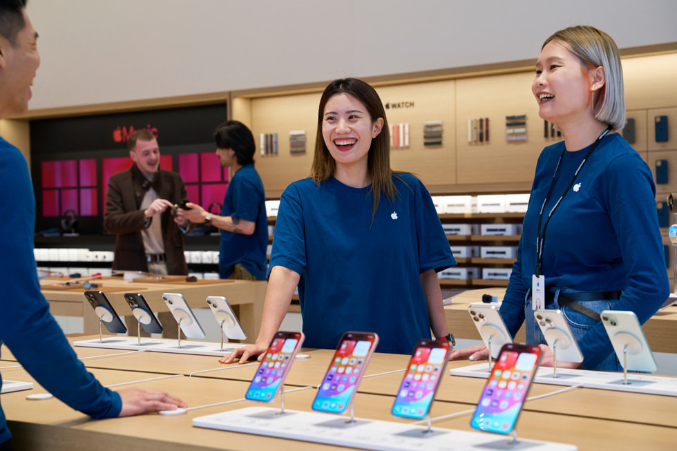 Three team members stand around a table displaying the latest iPhone family.