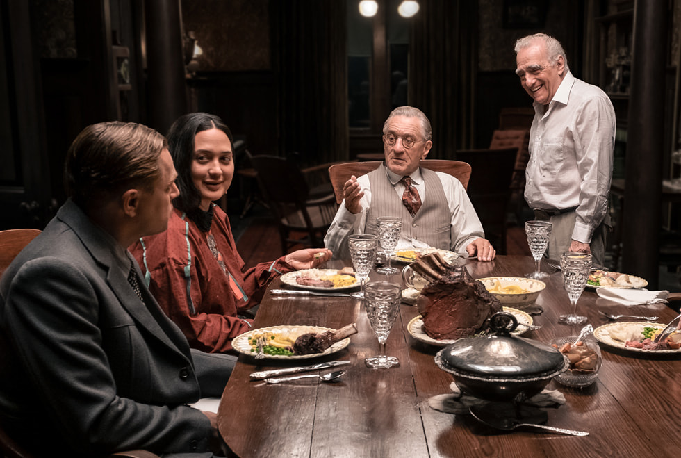 A behind-the-scenes still from “Killers of the Flower Moon” shows Leonardo DiCaprio, Lily Gladstone, Robert De Niro, and Martin Scorsese around a dining table.