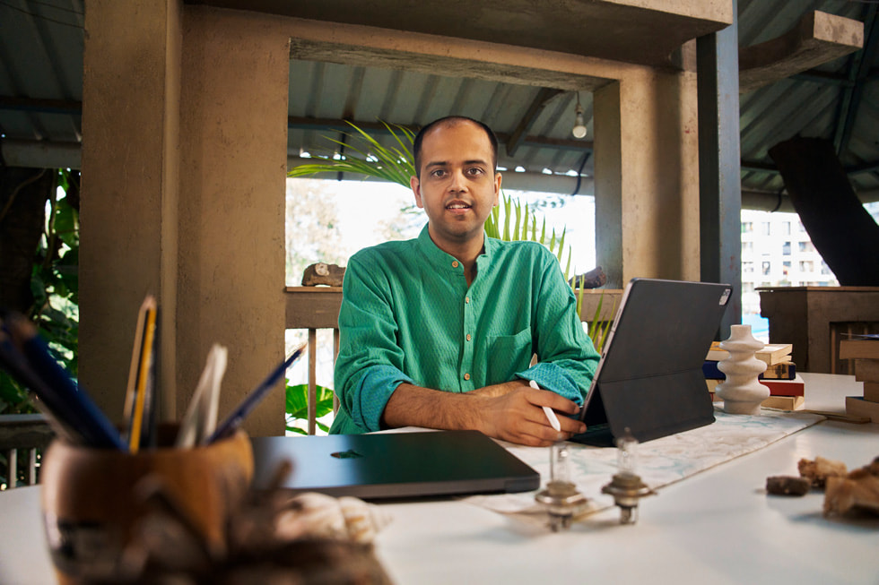 Dhruv Jani tenant un Apple Pencil, avec un iPad Pro et un MacBook Pro posés sur son bureau.