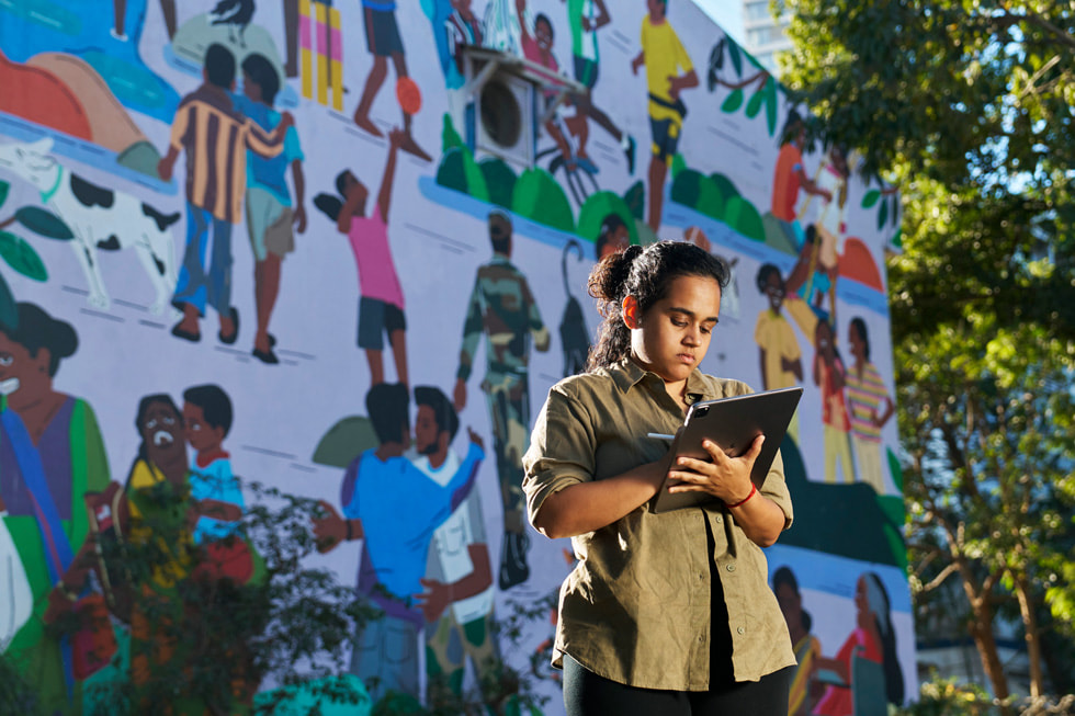 Sadhna Prasad using Apple Pencil with iPad Pro while standing in front of a large-scale mural.