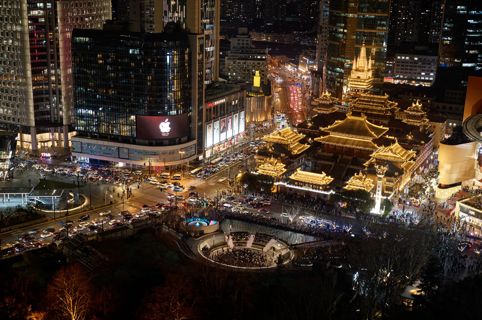 Exterior iluminado da Apple Jing’an, exibido à distância e à noite, perto do famoso Templo Jing'an.