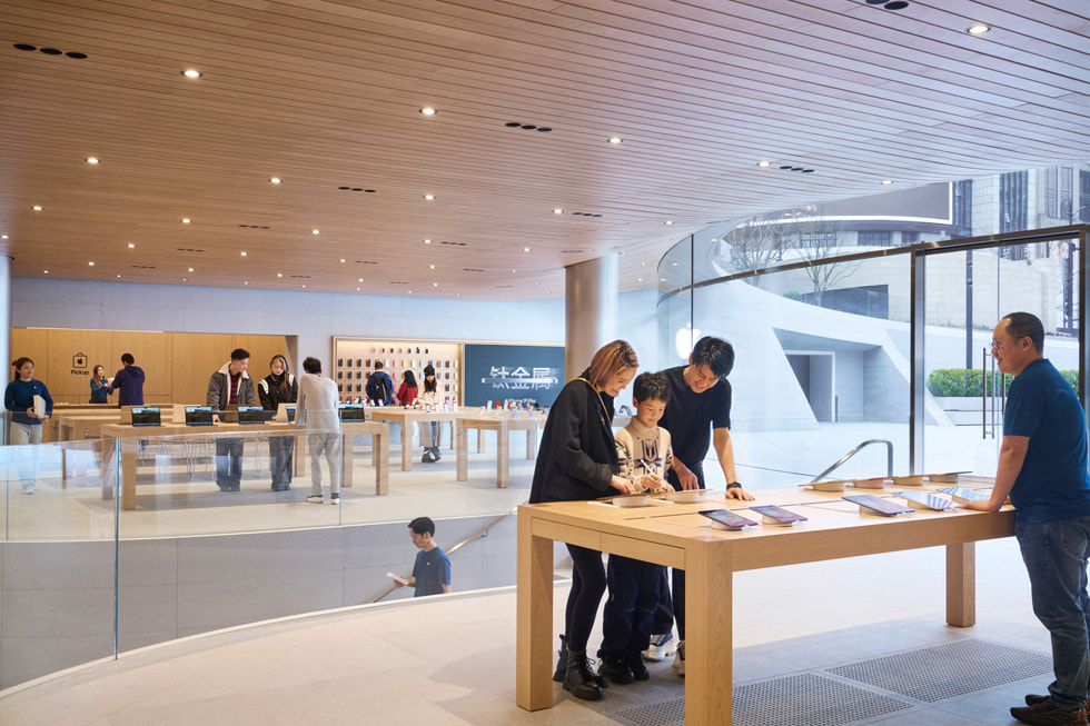Customers look at Apple products on a display table inside the store.