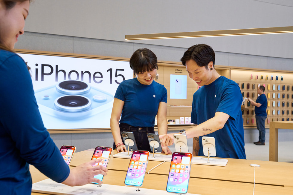 Team members look at iPhone 15 devices on a display table in the store.