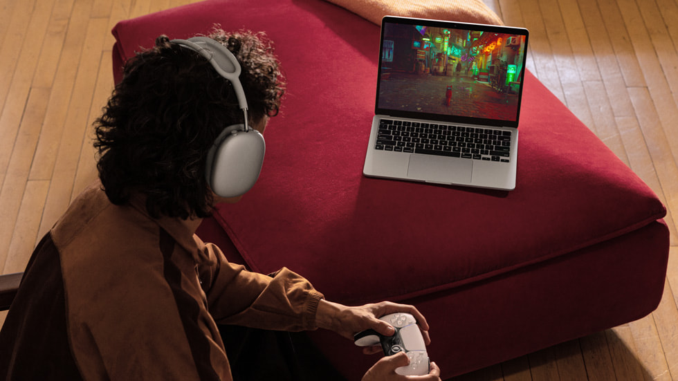ภาพบุคคลหนึ่งใส่หูฟังครอบศีรษะและกำลังเล่นเกมบน MacBook Air ใหม่