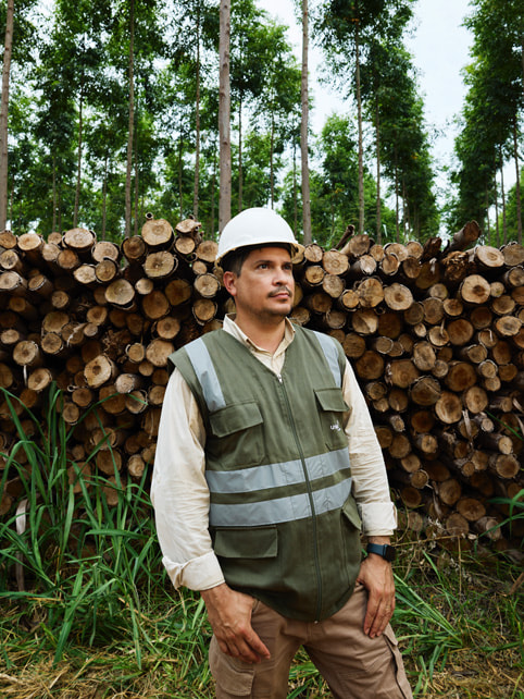 Alvaro Ramirez de pie frente a una pila de troncos.