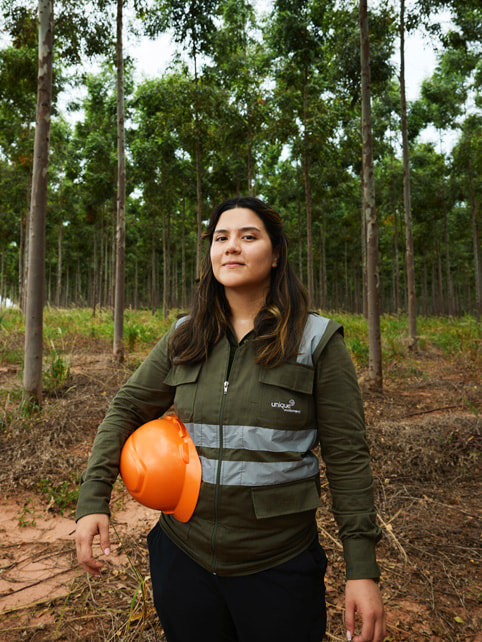 Belén Osario holds a hard hat while standing in the forest.