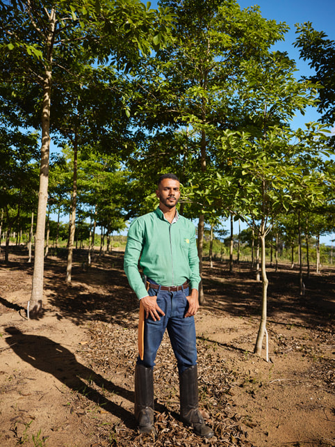 Victor Leon Rocha Araújo wears knee-high boots while standing among a row of trees in the Atlantic Forest.