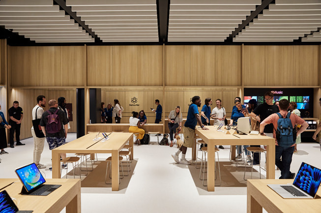 Una foto interior de un Apple Store con clientes y empleados hablando entre ellos.