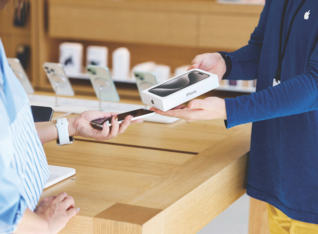 Image représentant Apple Trade In, où l’on voit une cliente échangeant son ancien téléphone contre un nouveau dans sa boîte.