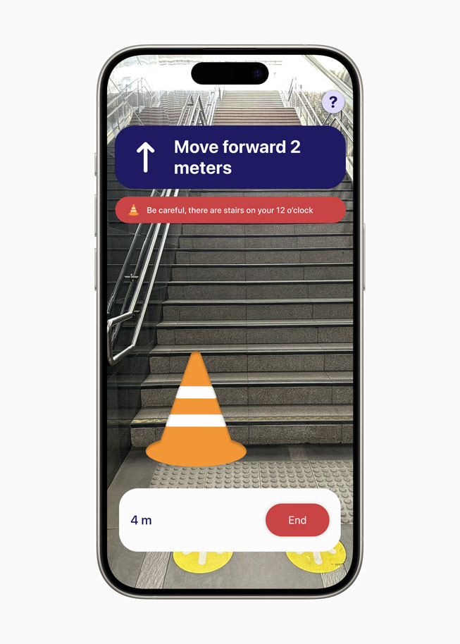 En skærm fra PetaNetra-appen på iPhone 15 Pro, med beskeden “Move forward 2 meters” og en note med teksten “Be careful, there are stairs on your 12 o’clock.” 