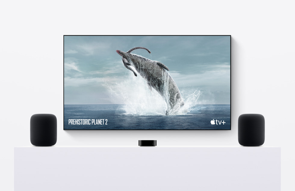 ลำโพง HomePod (รุ่นที่ 2) สองเครื่องวางอยู่ถัดจาก Apple TV ซึ่งกำลังเล่นสารคดีเรื่อง Prehistoric Planet จาก Apple TV+