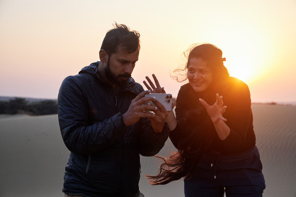 Archana Atul Phadke is shown with Amith Surendran, who holds iPhone 15 Pro Max, in a desert setting at sunset for Phadke’s film “Mirage.”