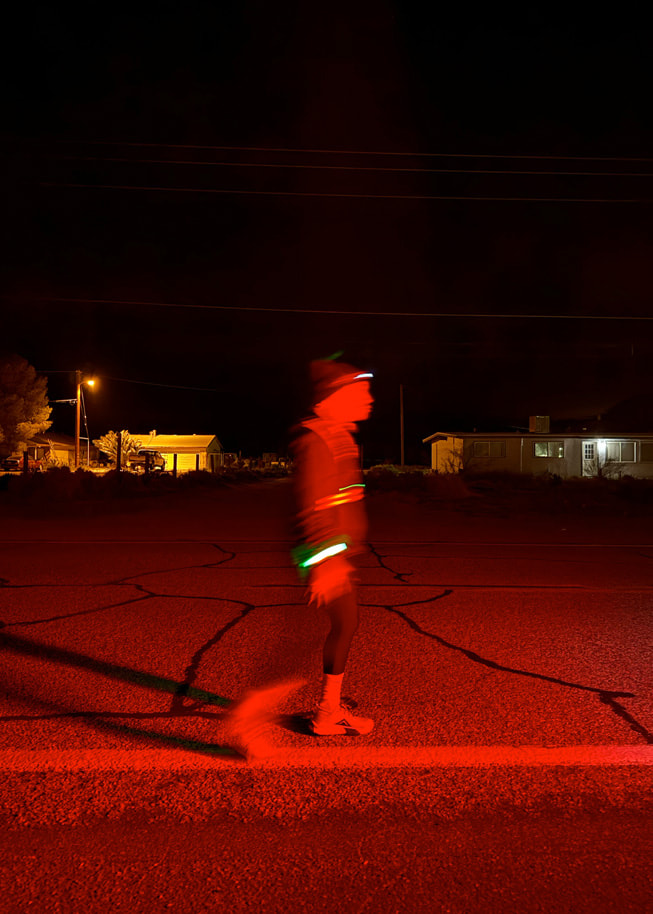 Un coureur portant un équipement réfléchissant photographié dans l’obscurité sur la route.