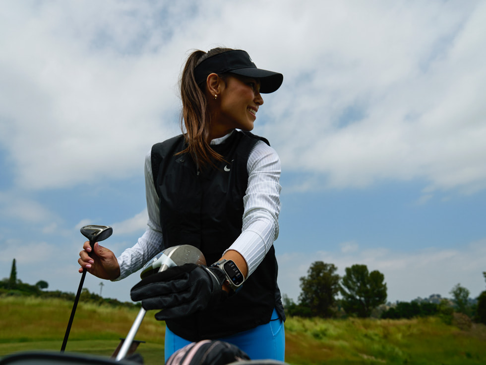 Imagen que muestra a una golfista sosteniendo dos palos de golf con un Apple Watch en la muñeca.