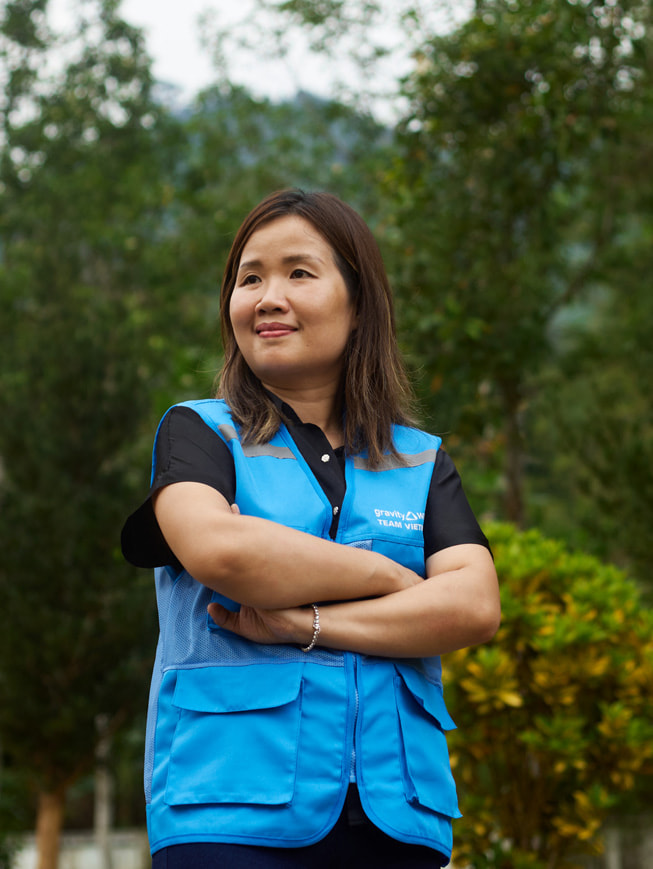 Portret Chu Thanh Hoa, która stoi na świeżym powietrzu i jest ubrana w niebieską kamizelkę z logo Gravity Water.