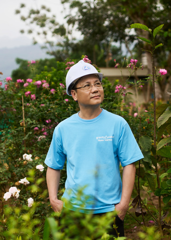 A portrait of Phan Viet Dung, standing outdoors against a backdrop of flowers and wearing a hard hat.