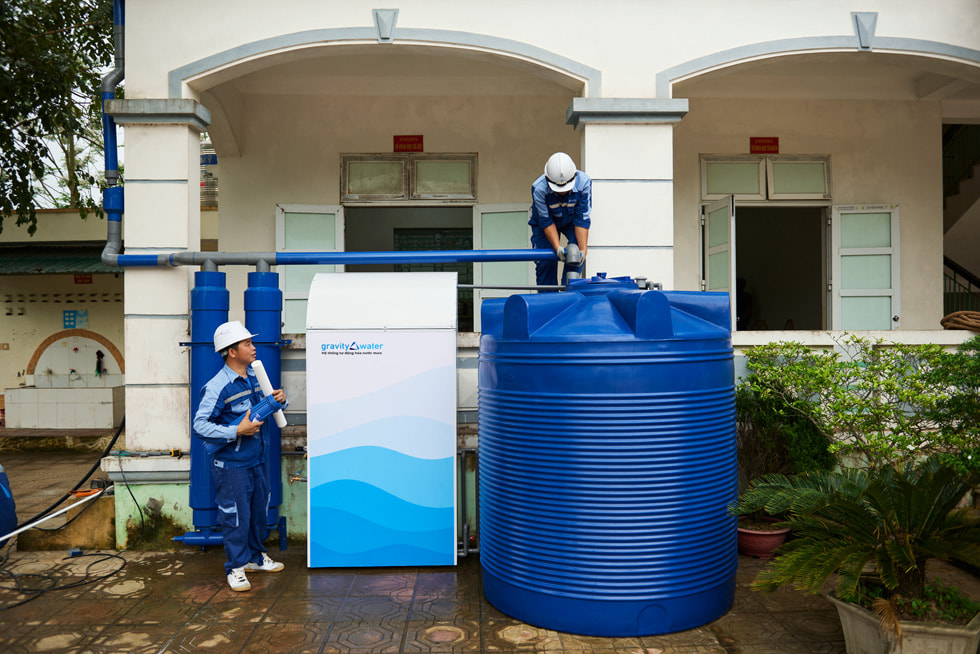 A person inspects the Gravity Water system while another person looks on.
