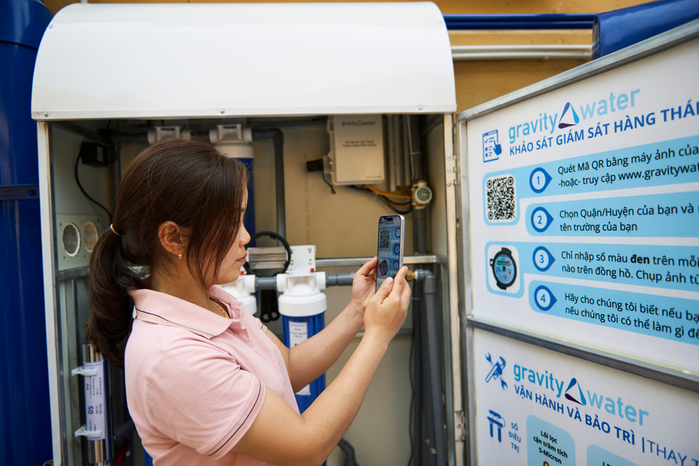 A student holds up an iPhone device to scan a QR code on Gravity Water signage at the Vay Nua Primary and Secondary Boarding School for Ethnic Minorities.