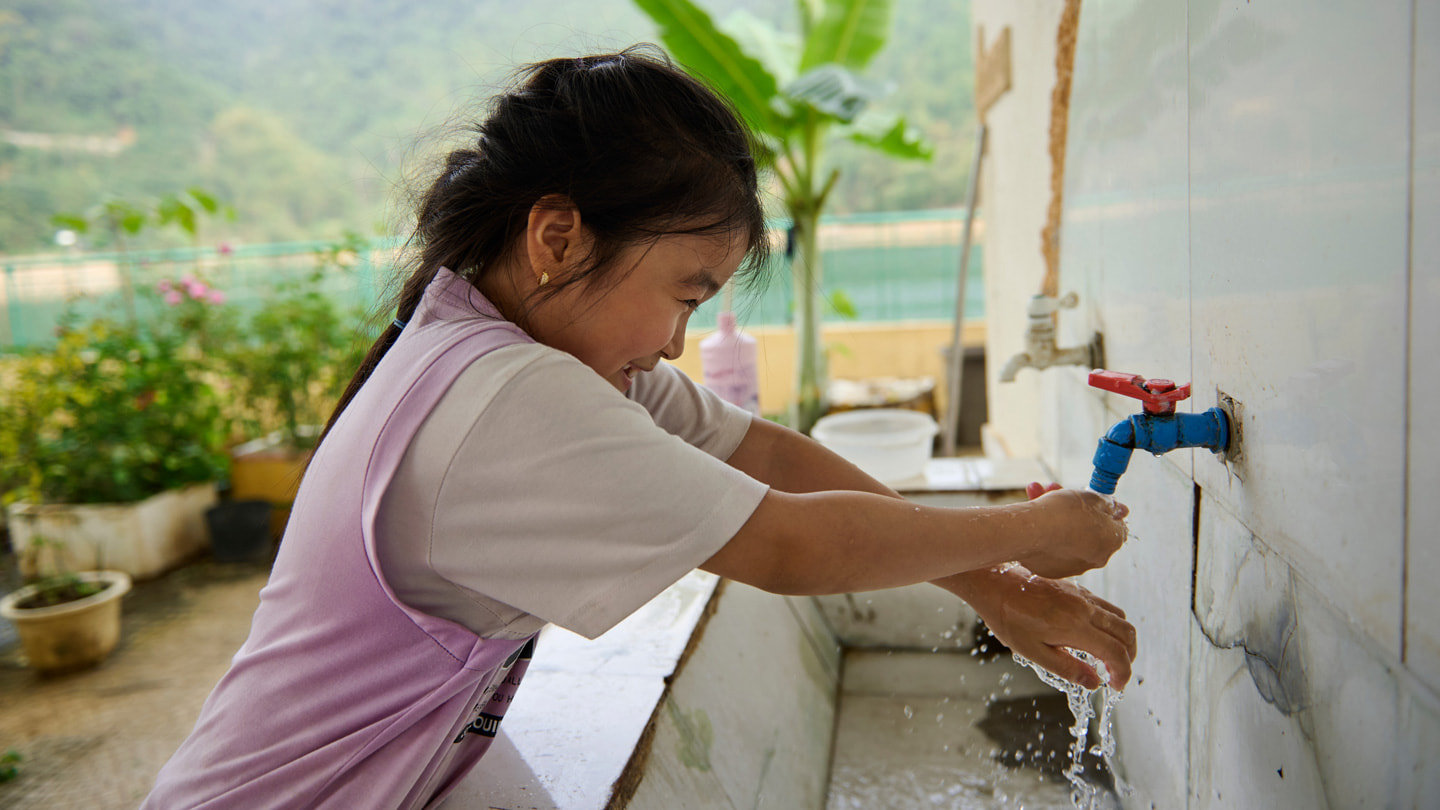 A student washes their hands outdoors in a large basin with a spigot at the Hiền Lương Primary and Secondary School.