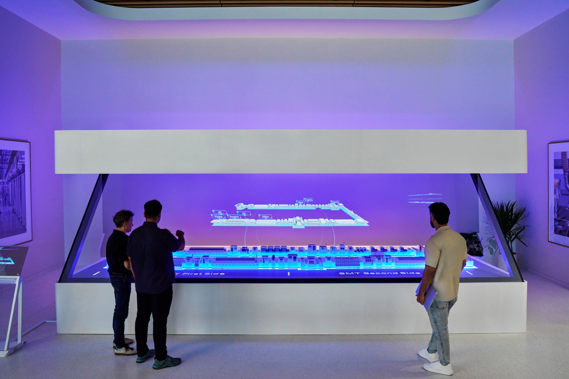 Appleのヒューストン製造研修拠点で、3人が光るホログラム台を囲む様子
