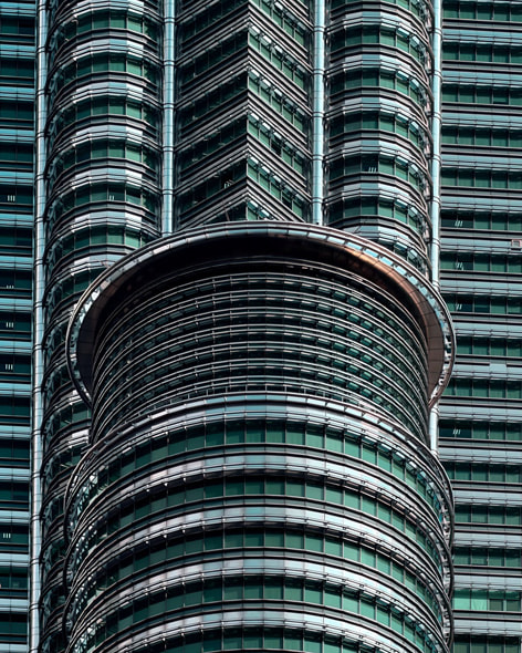 An angular close-up of part of twin skyscrapers in Kuala Lumpur, juxtaposed against a backdrop of cloudy blue sky.