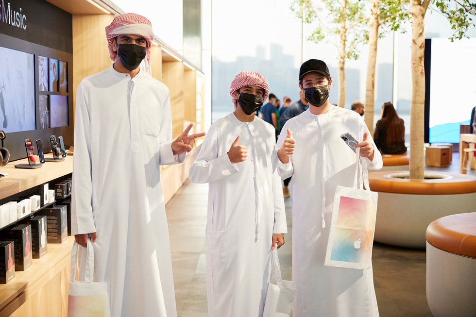 Three young customers showing their new purchases inside Apple Al Maryah Island.