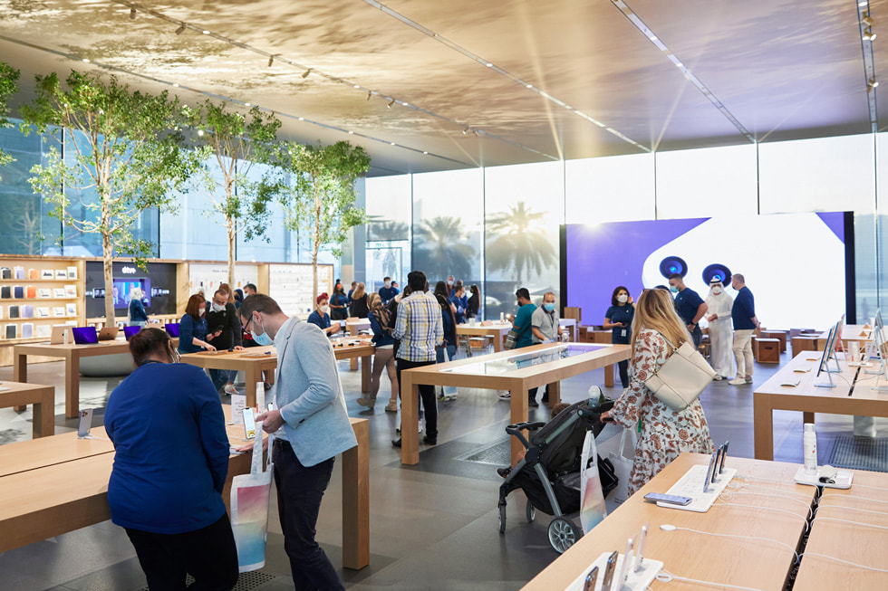 Inside Apple Al Maryah Island with customers and team members, with its unique ceiling of stretched gold fabric reflecting light.