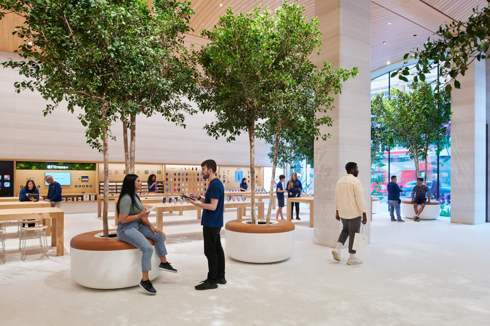 People converse by the Sicilian ficus tree planters inside Apple Brompton Road in London.