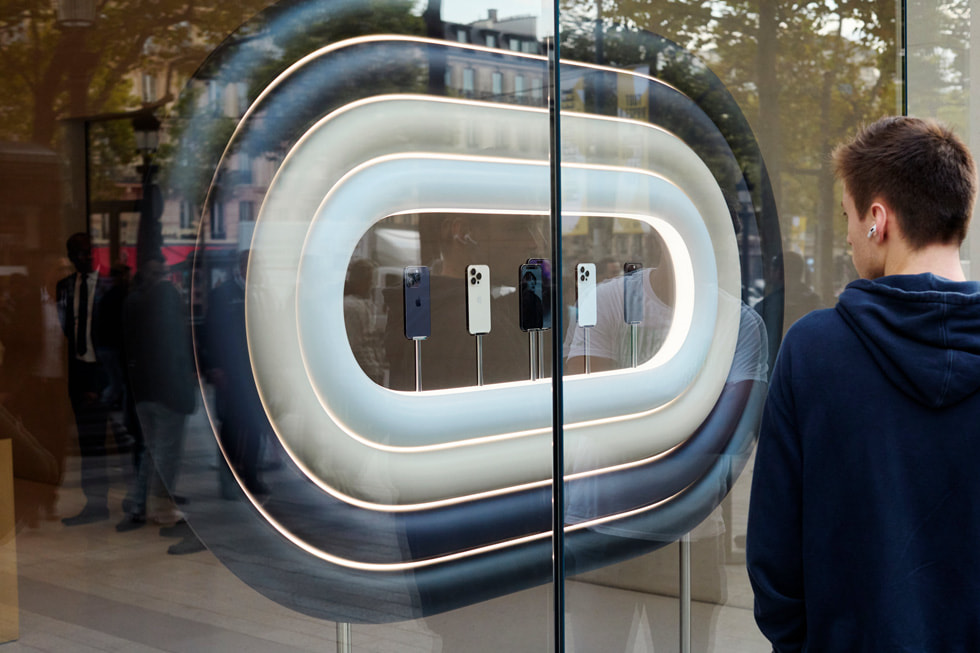 عميل في متجر Apple Champs-Élysées يمسك علبتين لجهازين من تشكيلة iPhone 14.