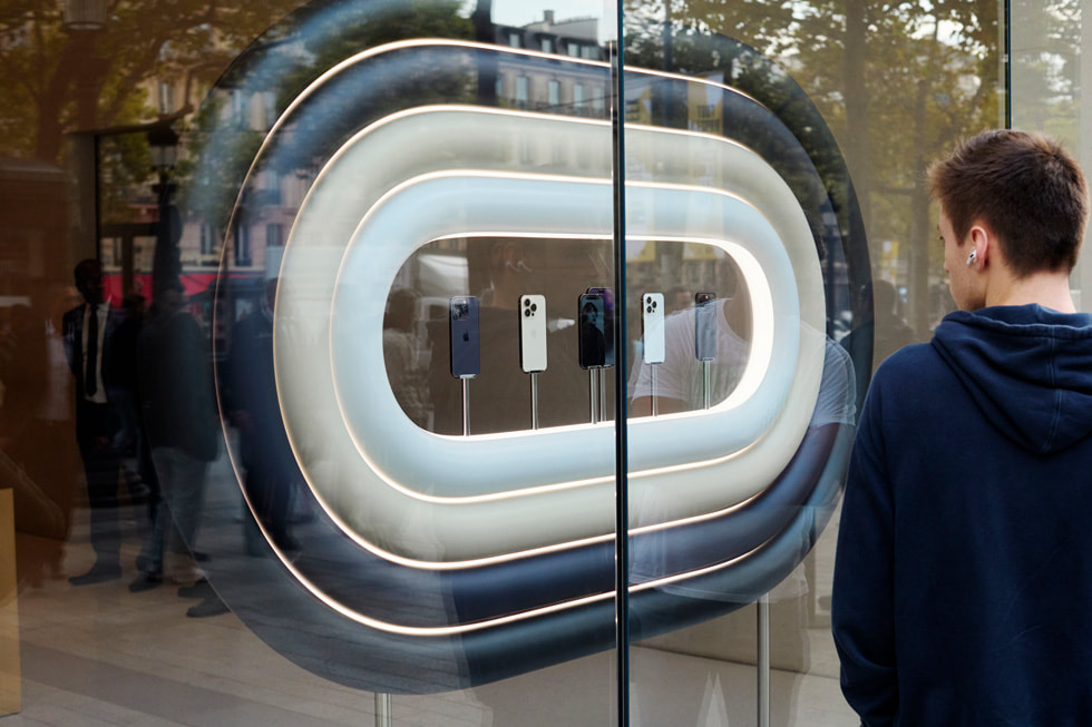 A customer at Apple Champs-Élysées holds up two boxed devices from the iPhone 14 line-up.