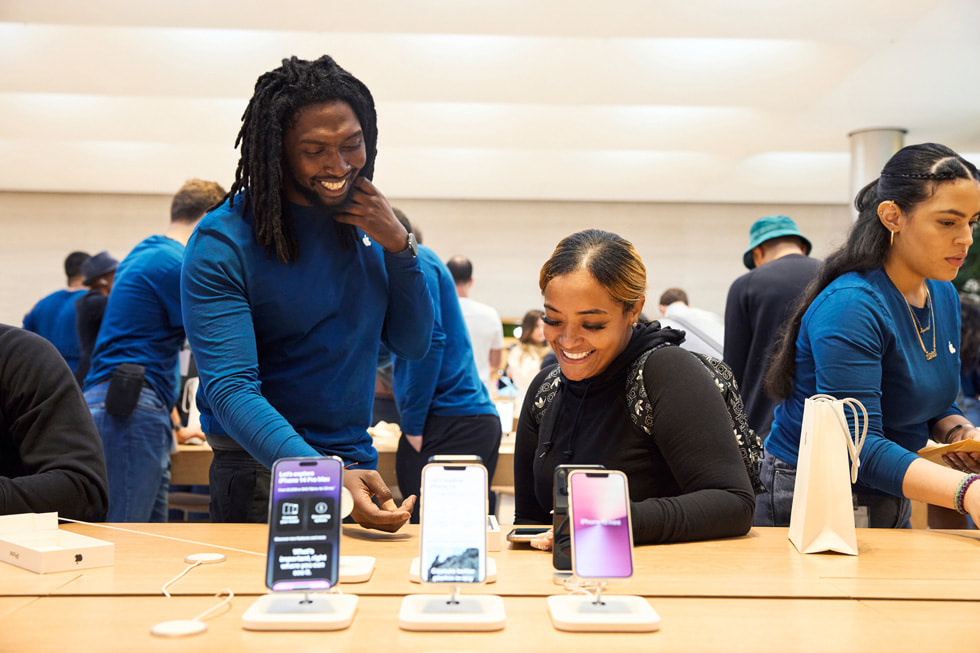 Een medewerker van Apple Fifth Avenue helpt een klant bij de displaytafel voor iPhone 14. 