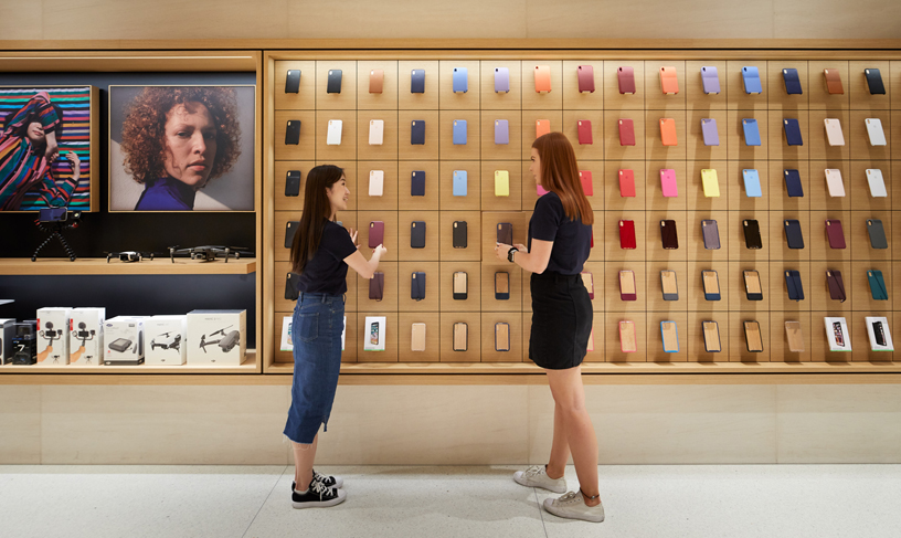 People standing in front of many iPhone cases displayed on wall.