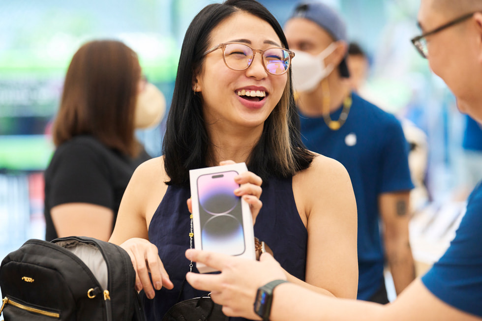 Een klant van Apple Orchard Road krijgt haar pas gekochte iPhone 14 Pro van een medewerker.