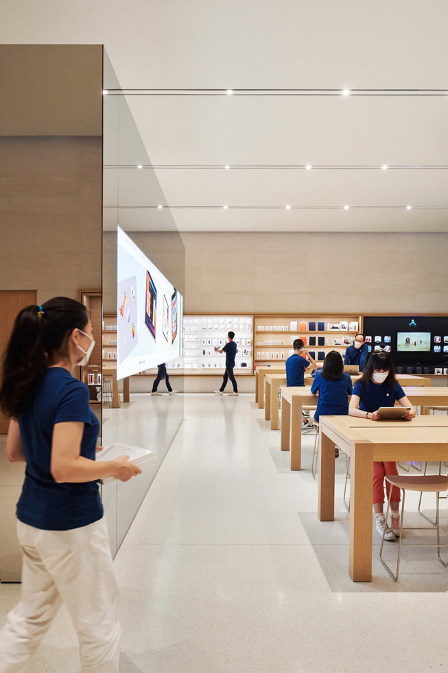 Eine Reihe von Tischen mit Mitarbeiter:innen des Retailteams und eine freistehende Videowand in Apple Changsha.
