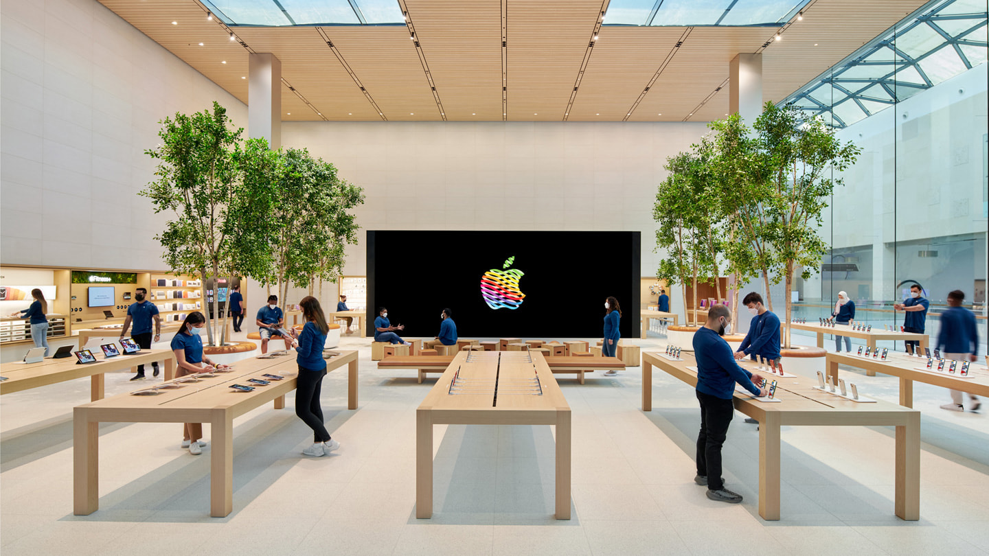 Внутри центра Apple Yas Mall с отдельно стоящей видеостеной и форумом, вокруг специалисты Apple.